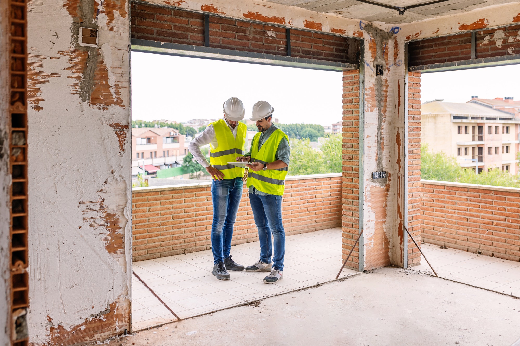Two adult construction architect men working on digital tablet at building site